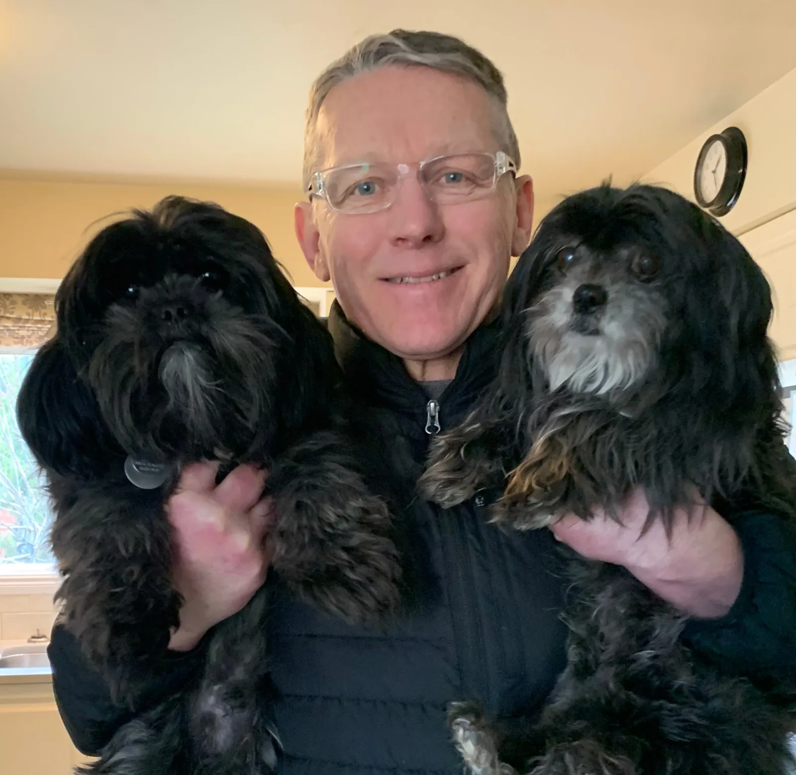Hans Anderssen smiling at home, holding his two small black dogs